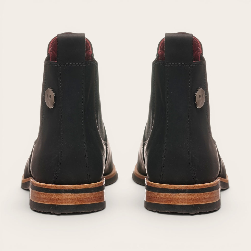 Botines chelsea negros de cuero para hombre OLKI con suela de cuero y caucho, con elásticos laterales. Detalle de pin metálico.