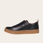 Zapatilla OLKI Calán negra de cuero con planta de caucho color cristal y detalle de lengüeta trasera.