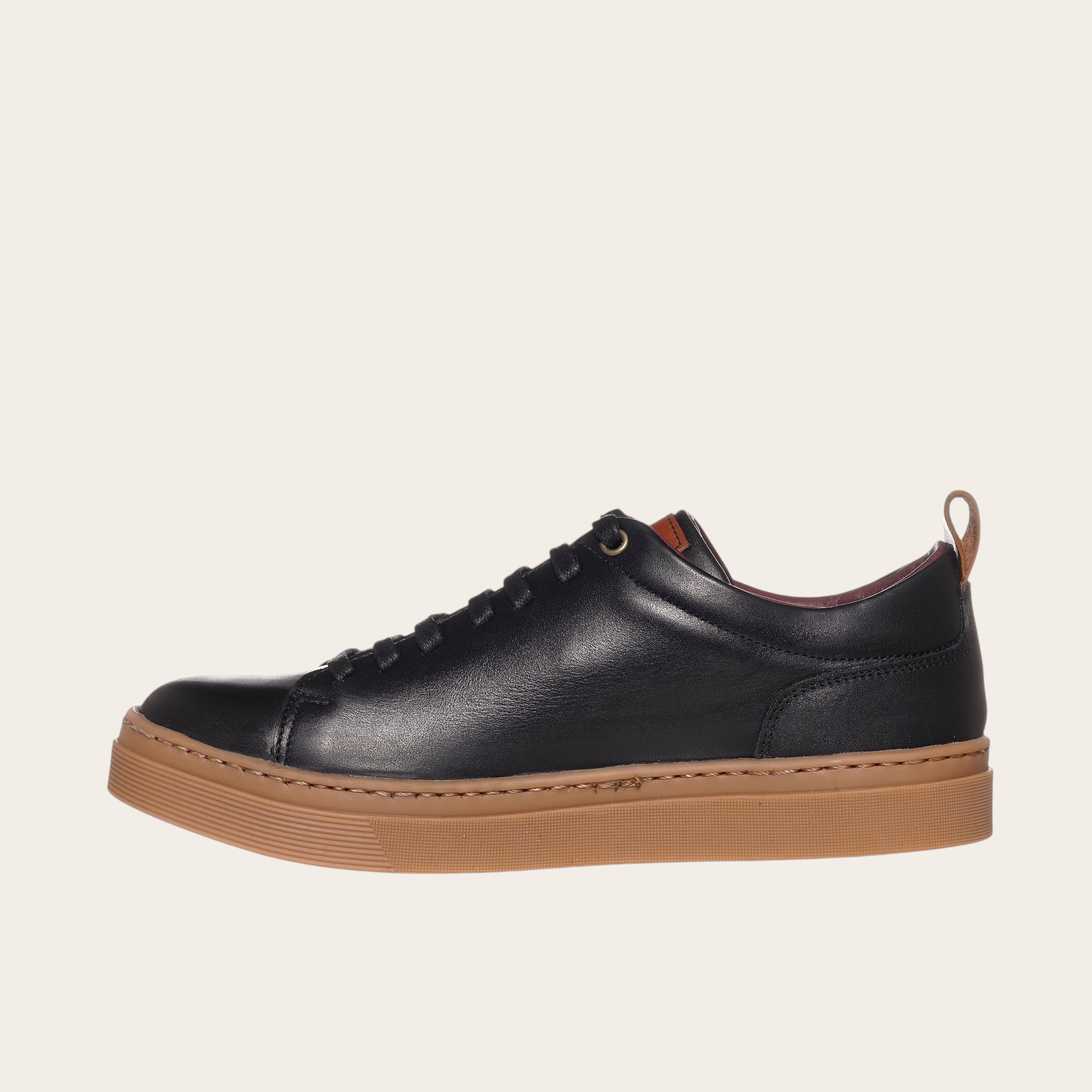 Zapatilla OLKI Calán negra de cuero con planta de caucho color cristal y detalle de lengüeta trasera.