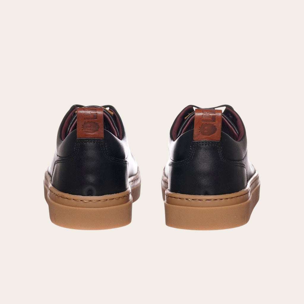 Zapatilla OLKI Calán negra de cuero con planta de caucho color cristal y detalle de logo en el talón.