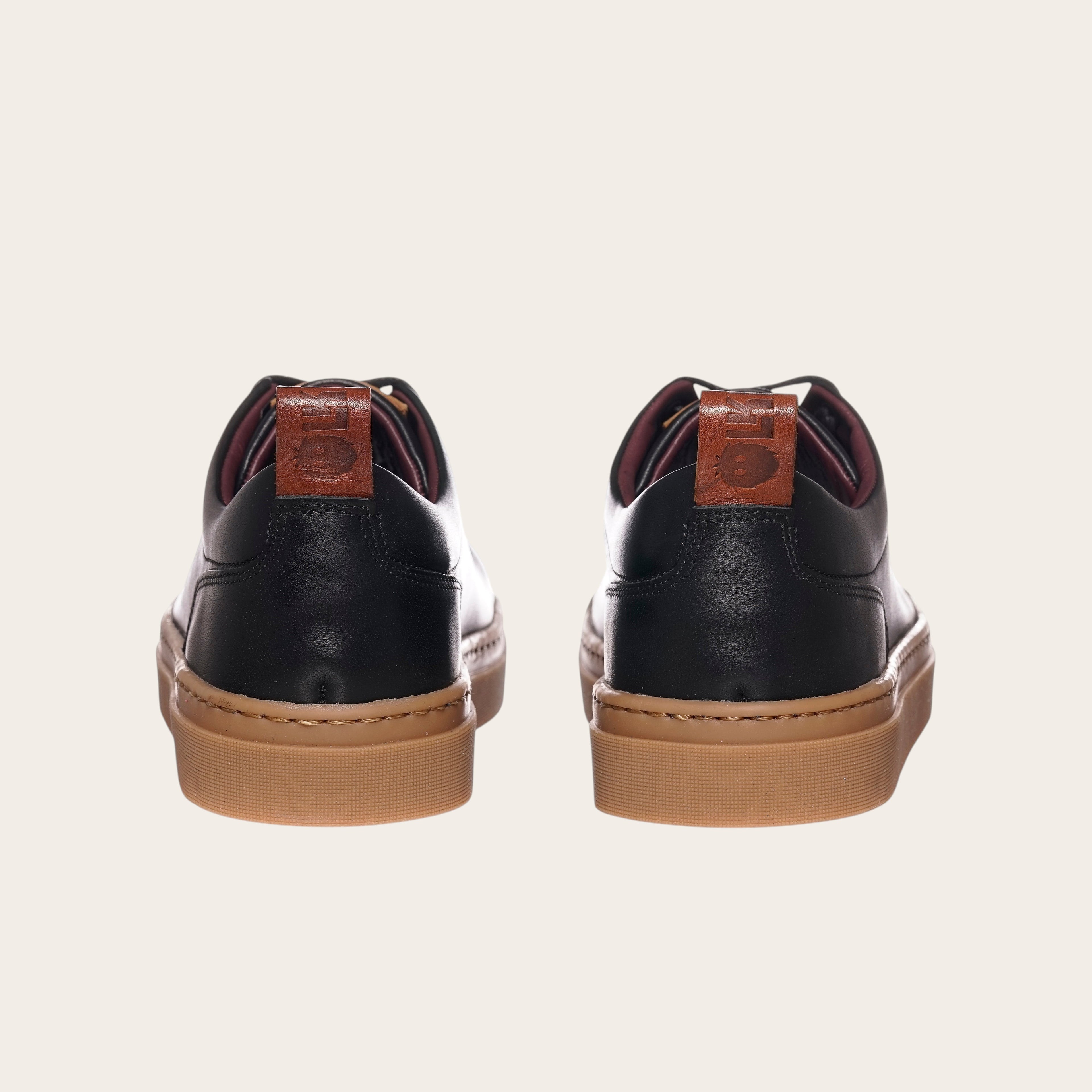 Zapatilla OLKI Calán negra de cuero con planta de caucho color cristal y detalle de logo en el talón.