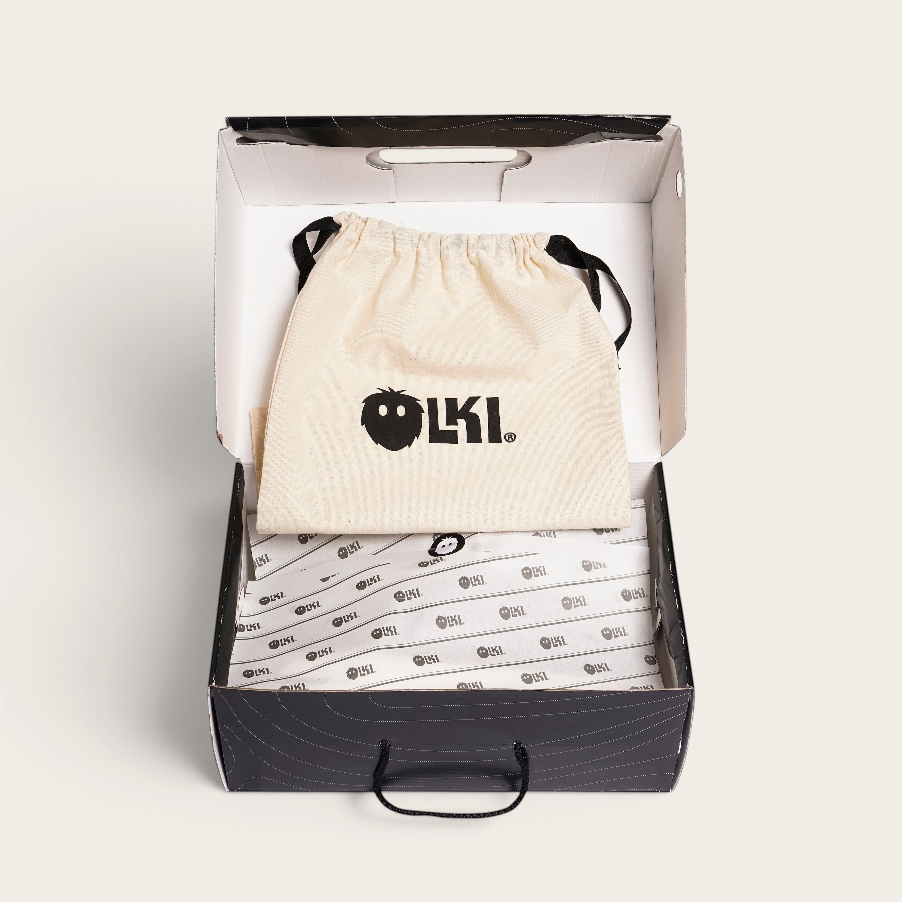 Zapatilla Calán negra de cuero de vacuno con cordones de algodón encerado y planta de caucho antideslizante, presentada en su caja con bolsa protectora. OLKI.