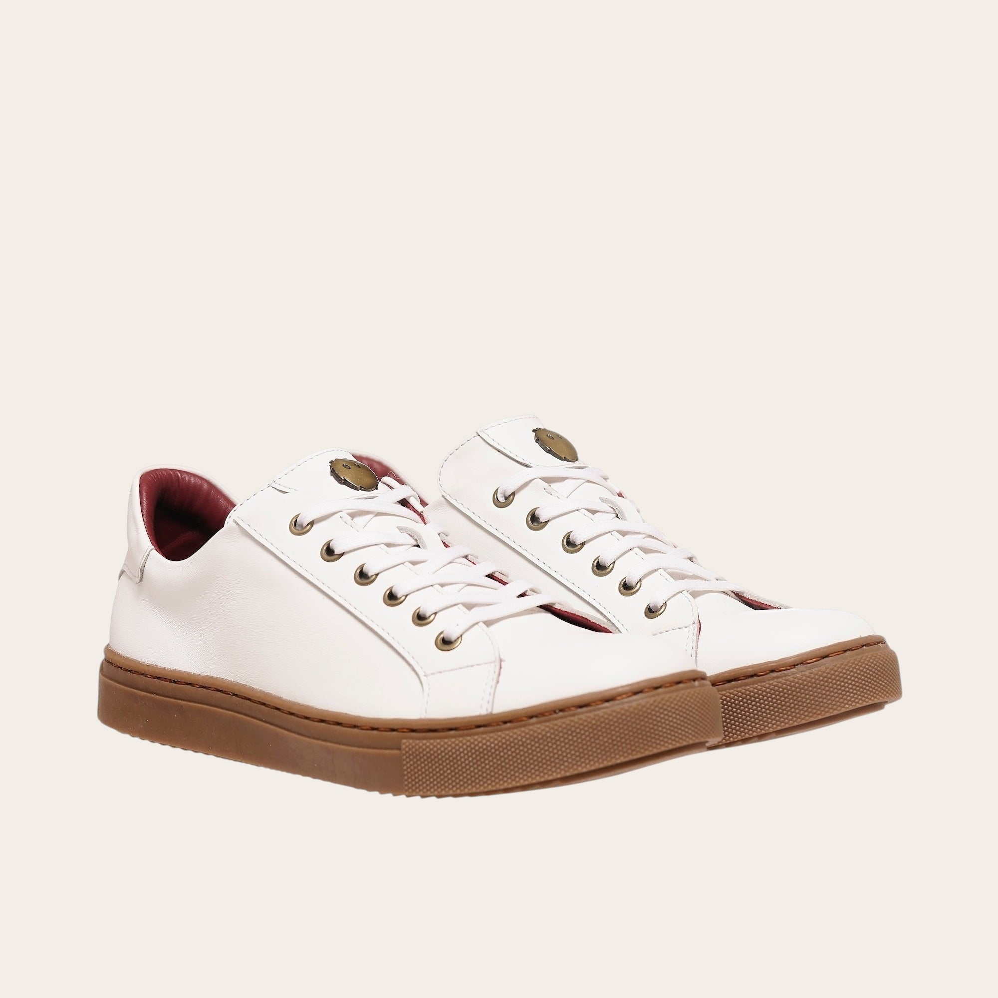 Zapatilla blanca de cuero de vacuno de OLKI con planta de caucho marrón y forro guinda. Diseño clásico con cordones.