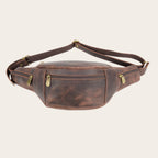 Banano OLKI de cuero natural vacuno en café oscuro con dos compartimentos y correa ajustable. Ideal para viajes.