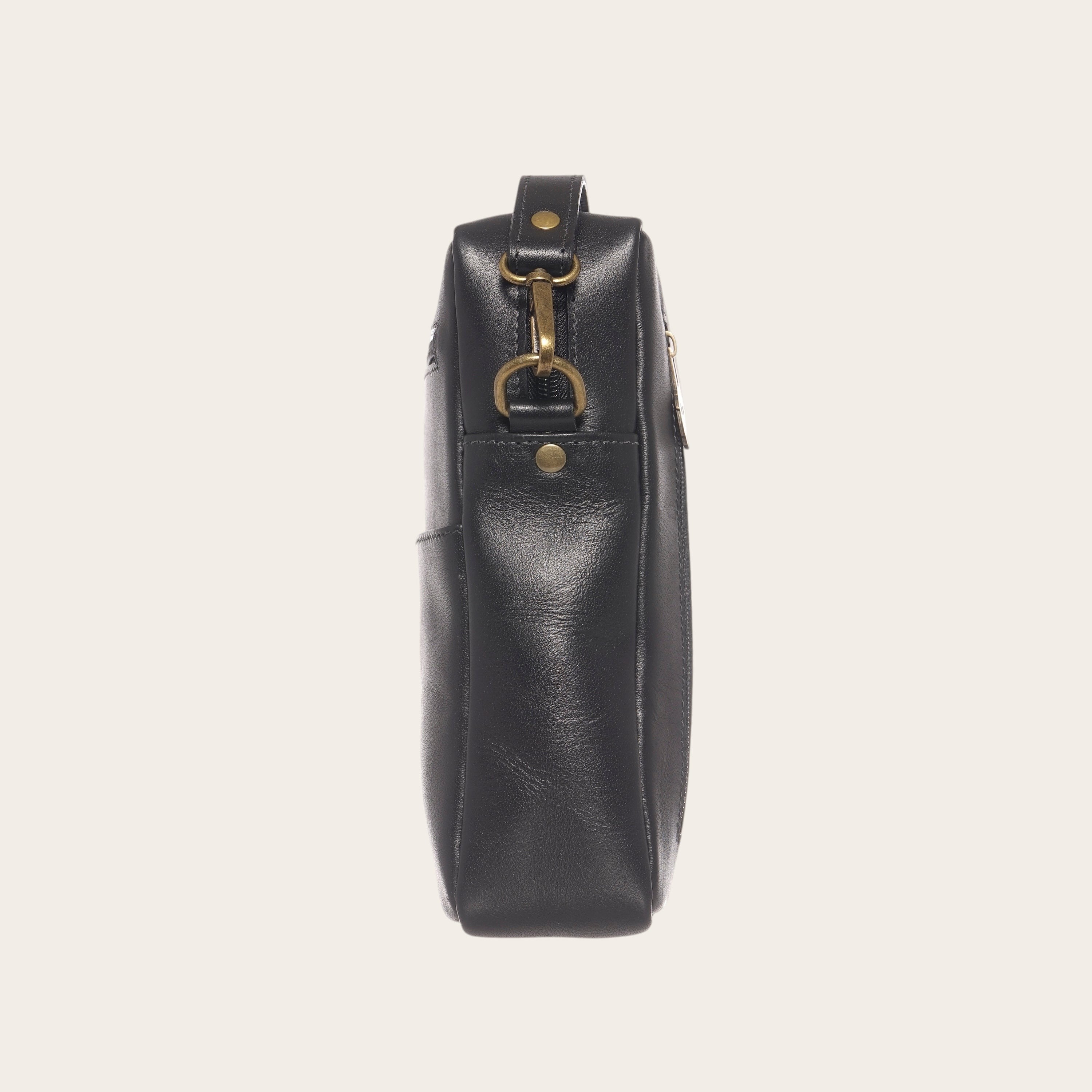 Bandolera negra de cuero natural OLKI Cautin con bolsillo exterior y herrajes dorados envejecidos.