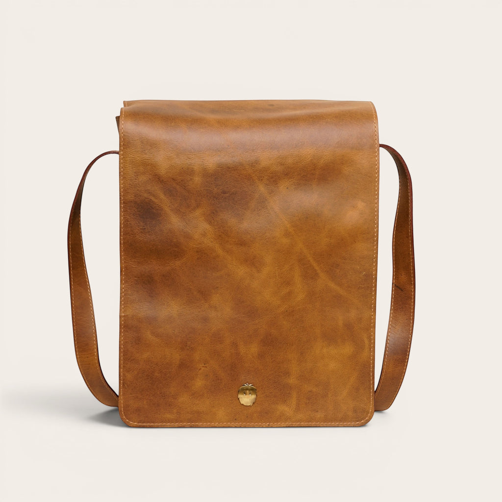 Bandolera vertical de cuero genuino OLKI en tono habano con solapa y broche metálico. Correa ajustable para hombre.