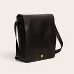 Bandolera negra texturizada de cuero OLKI con solapa y detalle metálico dorado. Correa ajustable para llevar cruzada o al hombro.
