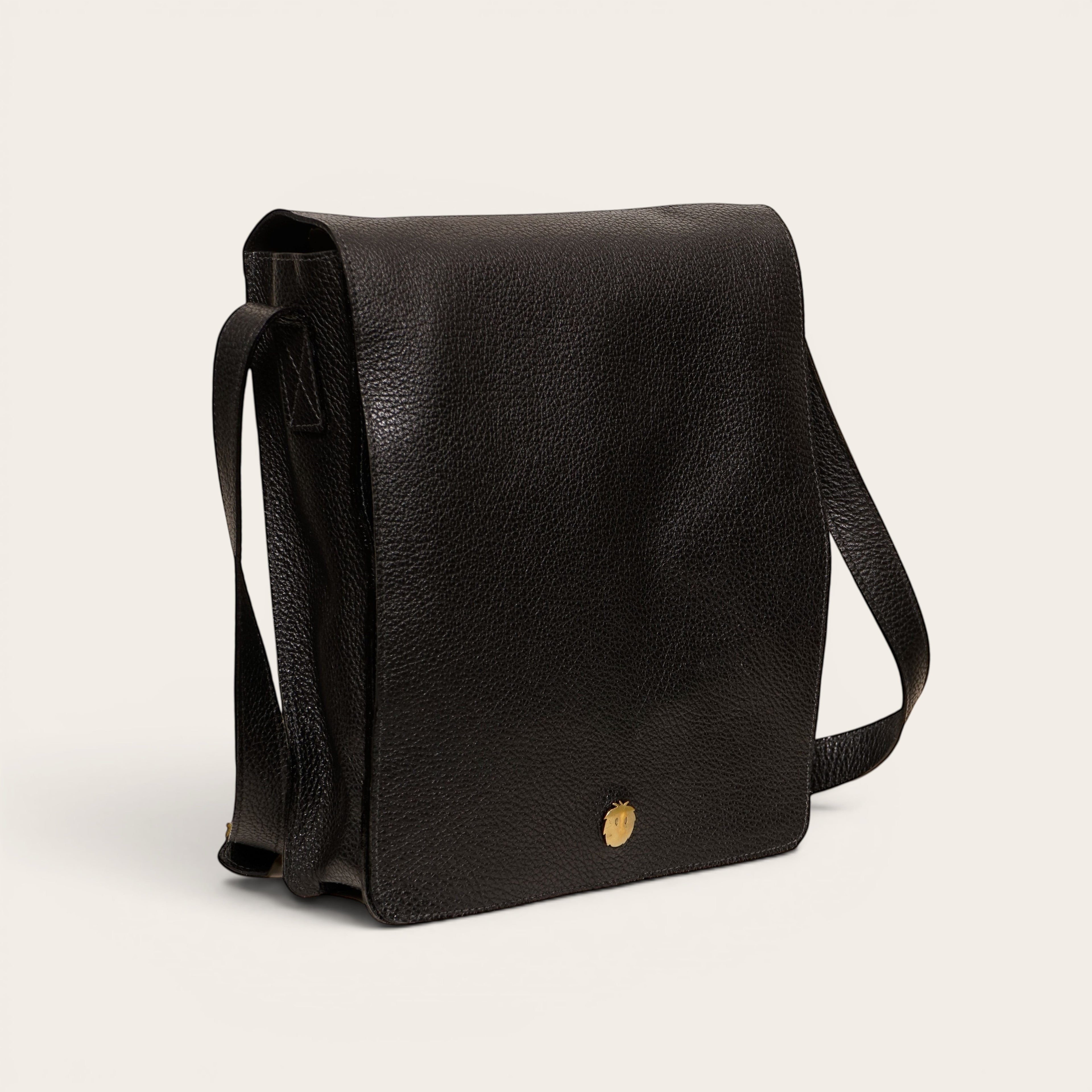 Bandolera negra texturizada de cuero OLKI con solapa y detalle metálico dorado. Correa ajustable para llevar cruzada o al hombro.