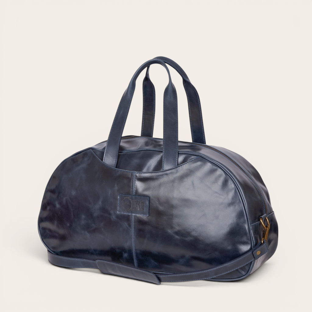 Bolso de viaje Baker azul marino de cuero de OLKI con asas superiores y correa desmontable, diseño clásico.