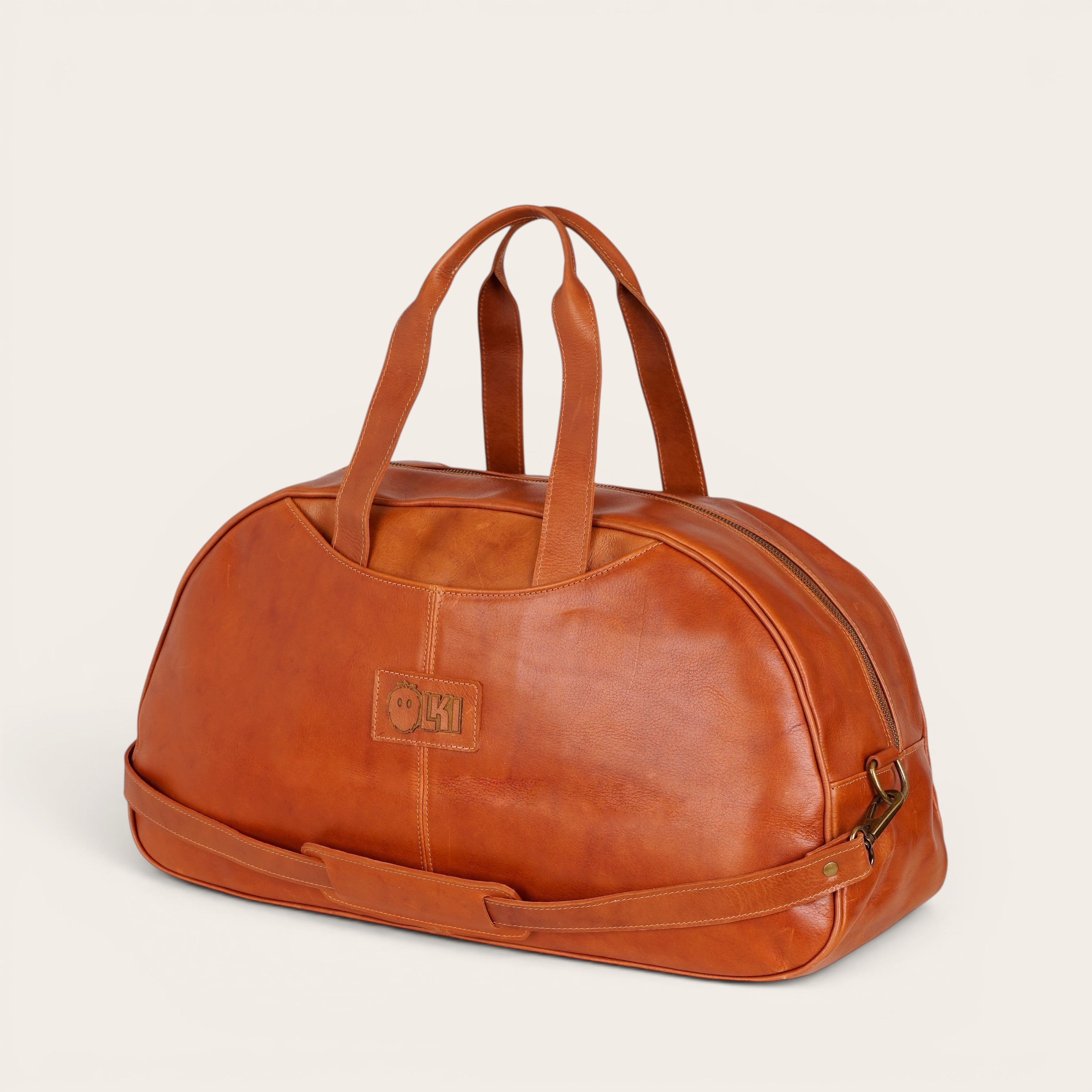 Bolso de viaje Baker Curry de cuero natural de vacuno de OLKI con asas y correa ajustable. Bolsillos interiores y exteriores, costuras reforzadas y herrajes envejecidos.