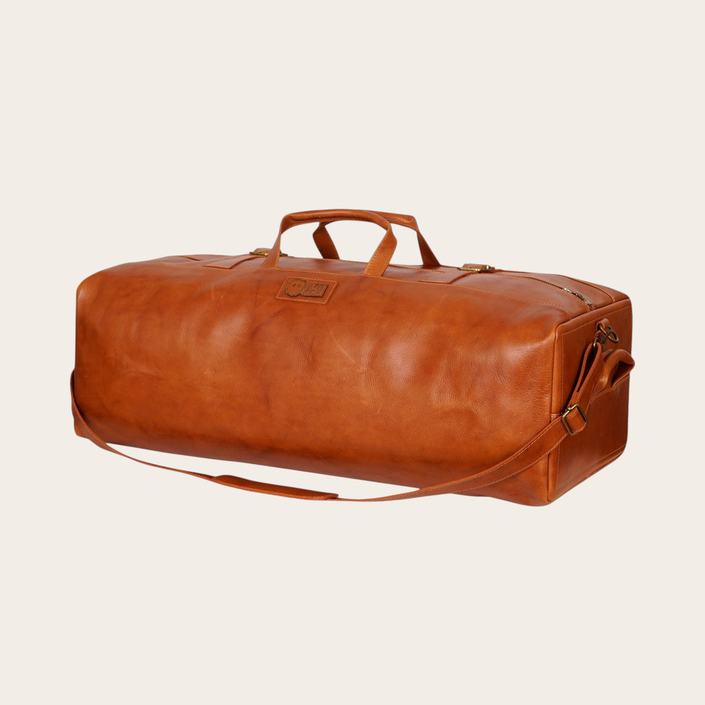 Bolso de viaje OLKI Yelcho en cuero color curry, con asas de mano y correa ajustable para el hombro.