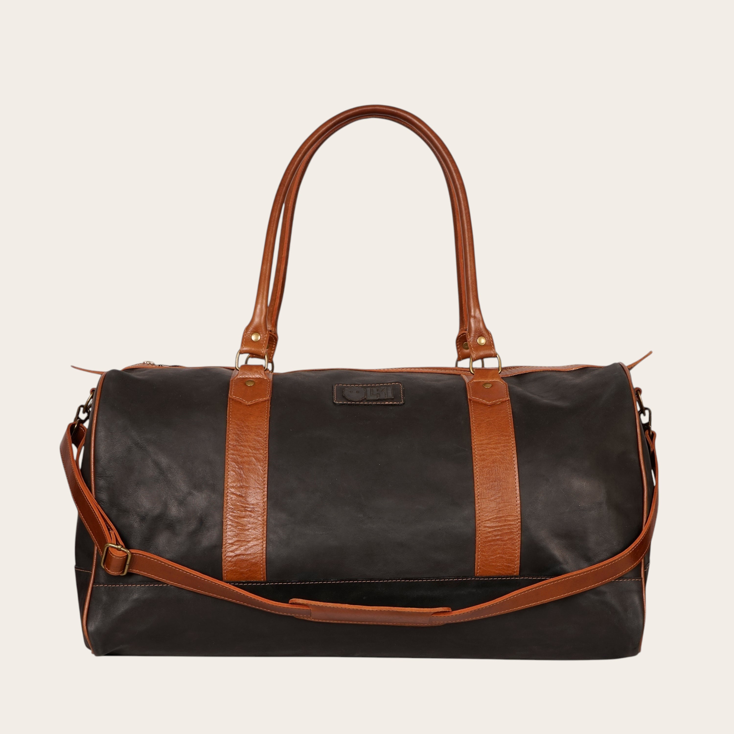 Bolso de viaje OLKI Futaleufu negro y marrón de cuero, con asas y correa de hombro, cierres metálicos envejecidos y costuras reforzadas.