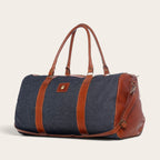 Bolso de viaje OLKI Futaleufú en mezclilla azul con detalles de cuero marrón, asas superiores y correa ajustable.