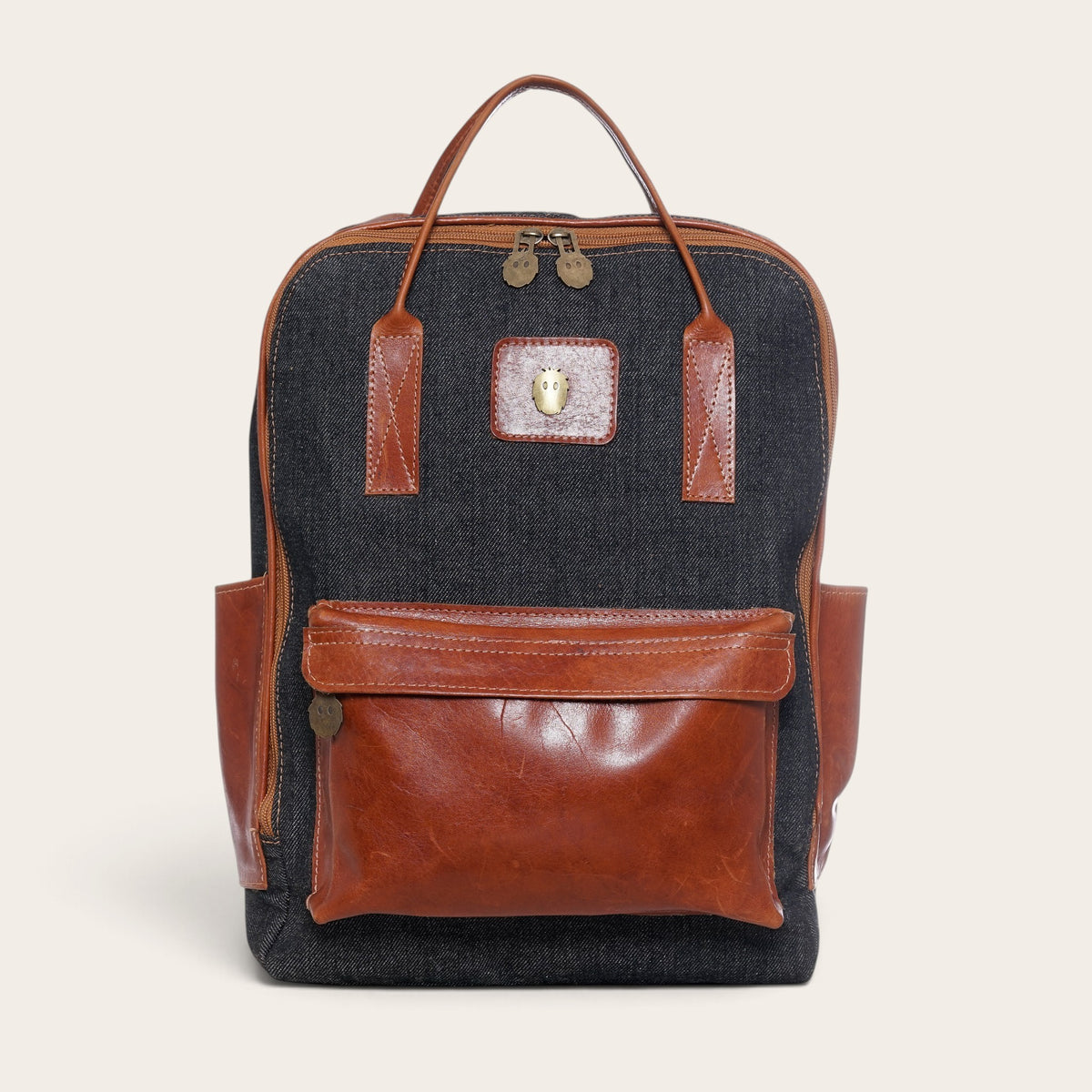Mochila OLKI Caliboro de mezclilla gris con detalles de cuero marrón, bolsillo frontal y asas superiores.