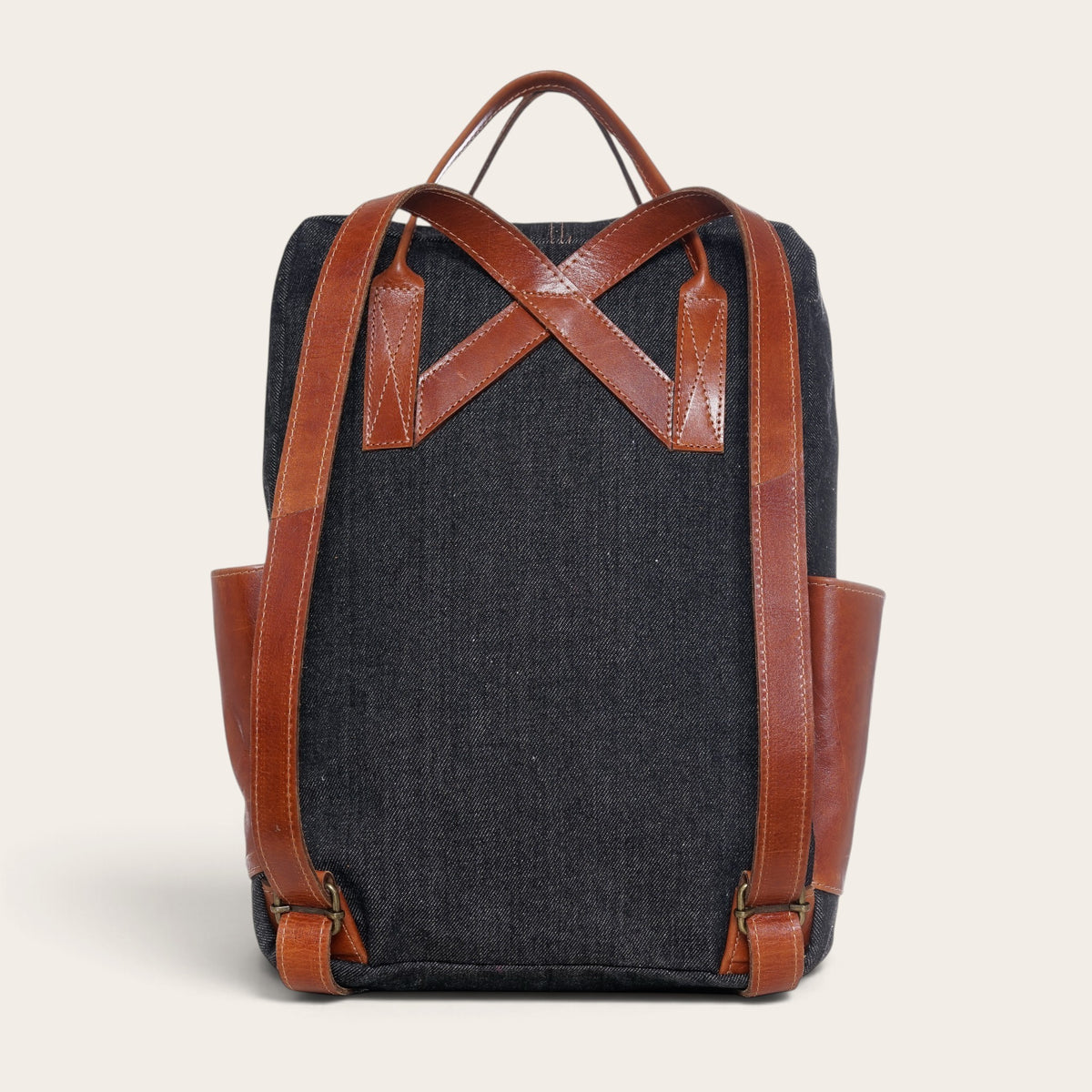 Mochila OLKI Caliboro de mezclilla gris con correas y detalles en cuero marrón, vista trasera.