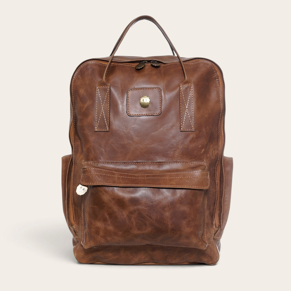 Mochila OLKI Caliboro de cuero natural color café con diseño compacto, bolsillo frontal y asas superiores.