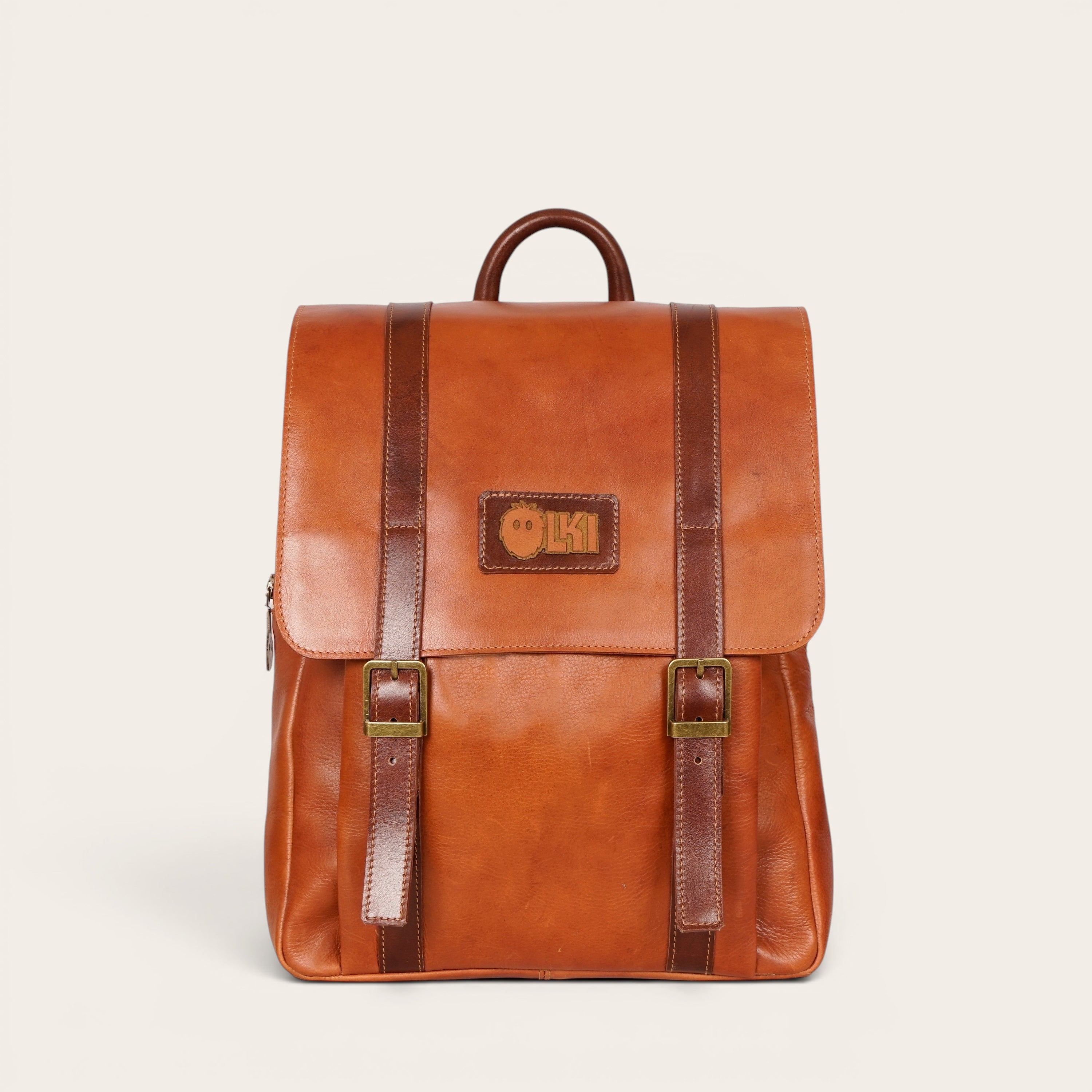 Mochila Trancura Curry de cuero natural de vacuno en color coñac con correas y hebillas de cuero marrón. Logo de OLKI en la solapa.
