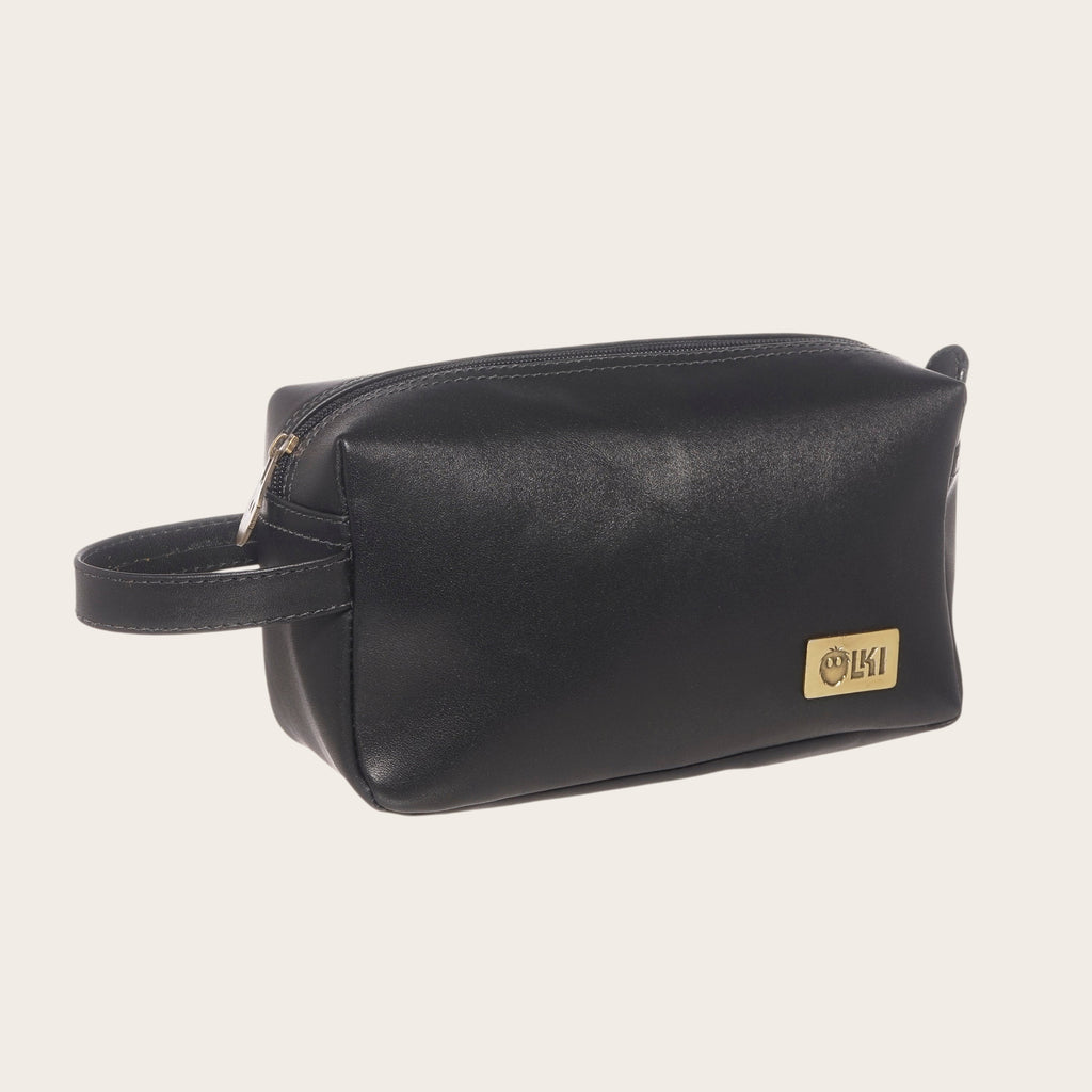 Neceser de cuero negro de OLKI con asa lateral y placa dorada, ideal para viajes y uso diario.