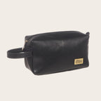 Neceser de cuero negro de OLKI con asa lateral y placa dorada, ideal para viajes y uso diario.
