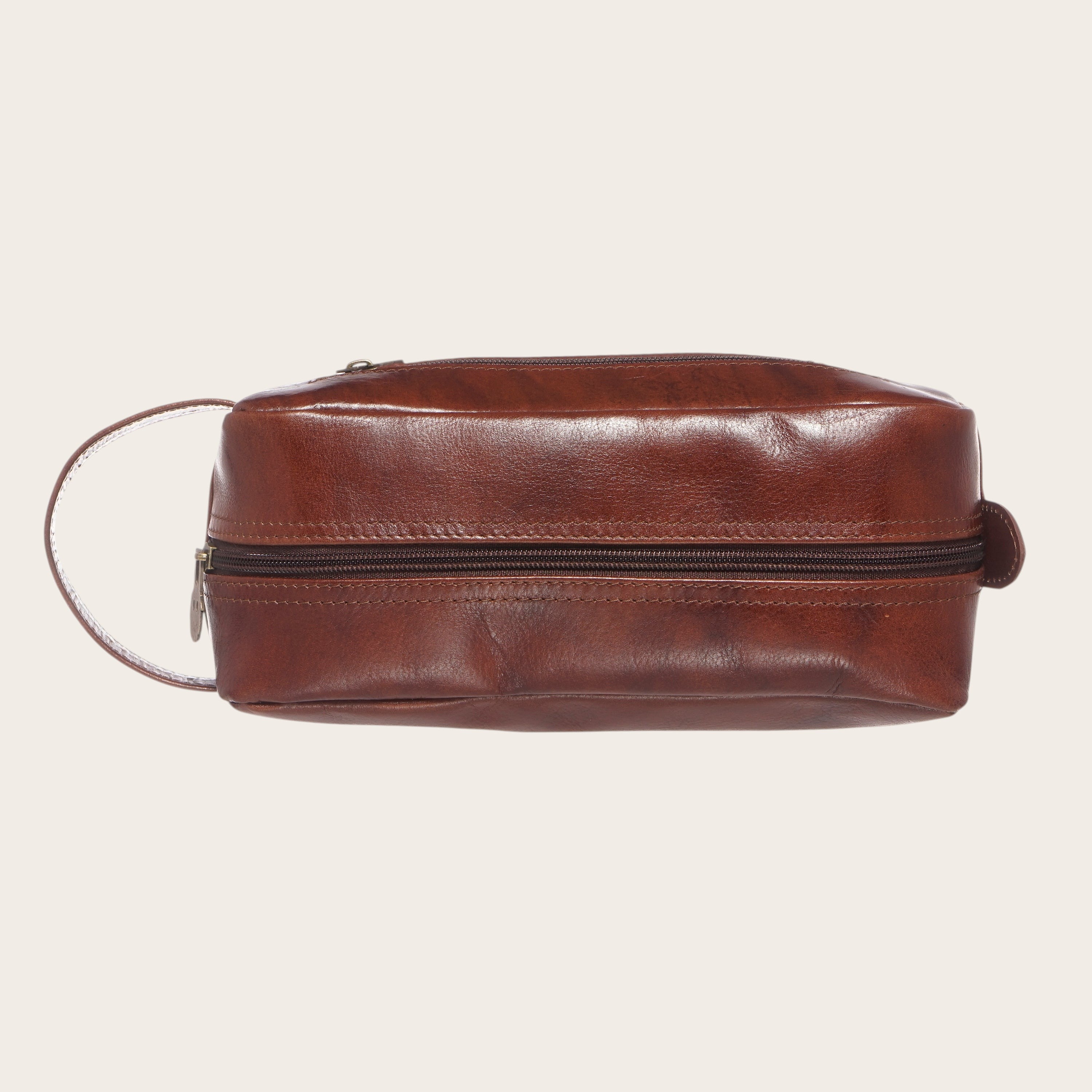 Neceser Loa Castaño de cuero de vacuno liso y brillante en tono castaño de OLKI, con asa lateral y cremallera.