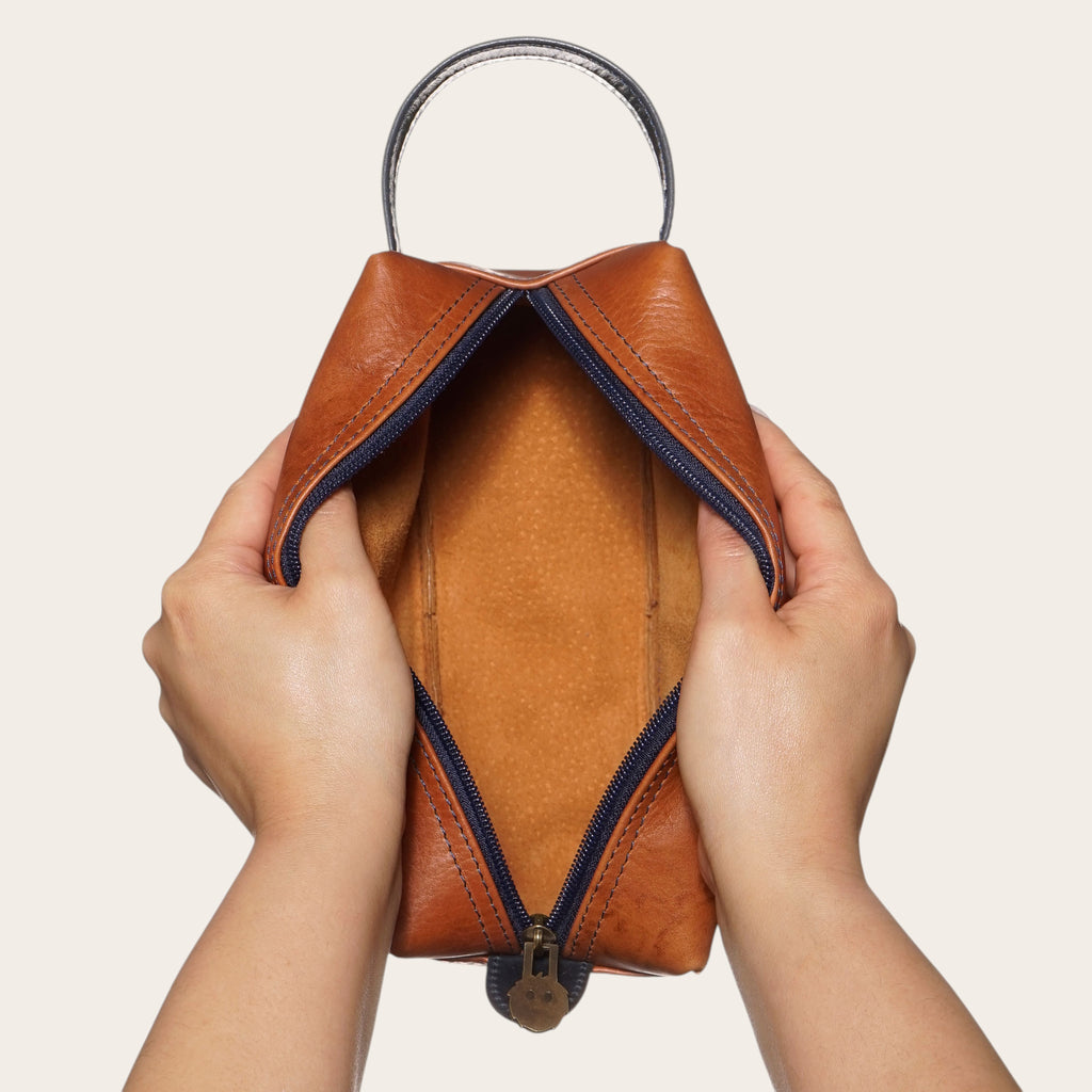 Neceser Elqui de cuero tostado y azul de OLKI, con asa y cremallera, ideal para viajes.