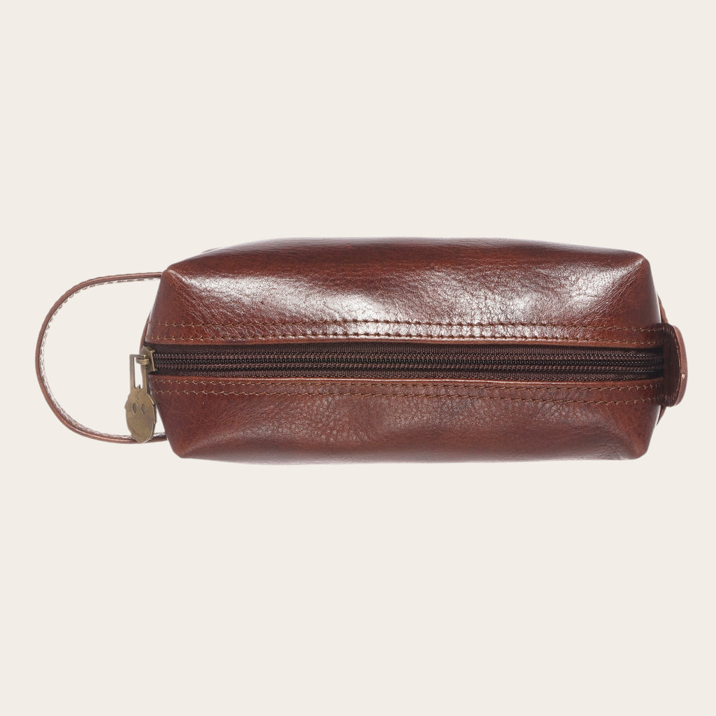 Neceser Lluta Castaño de cuero marrón de OLKI con asa lateral y cremallera dorada. Ideal para organizar artículos de aseo.