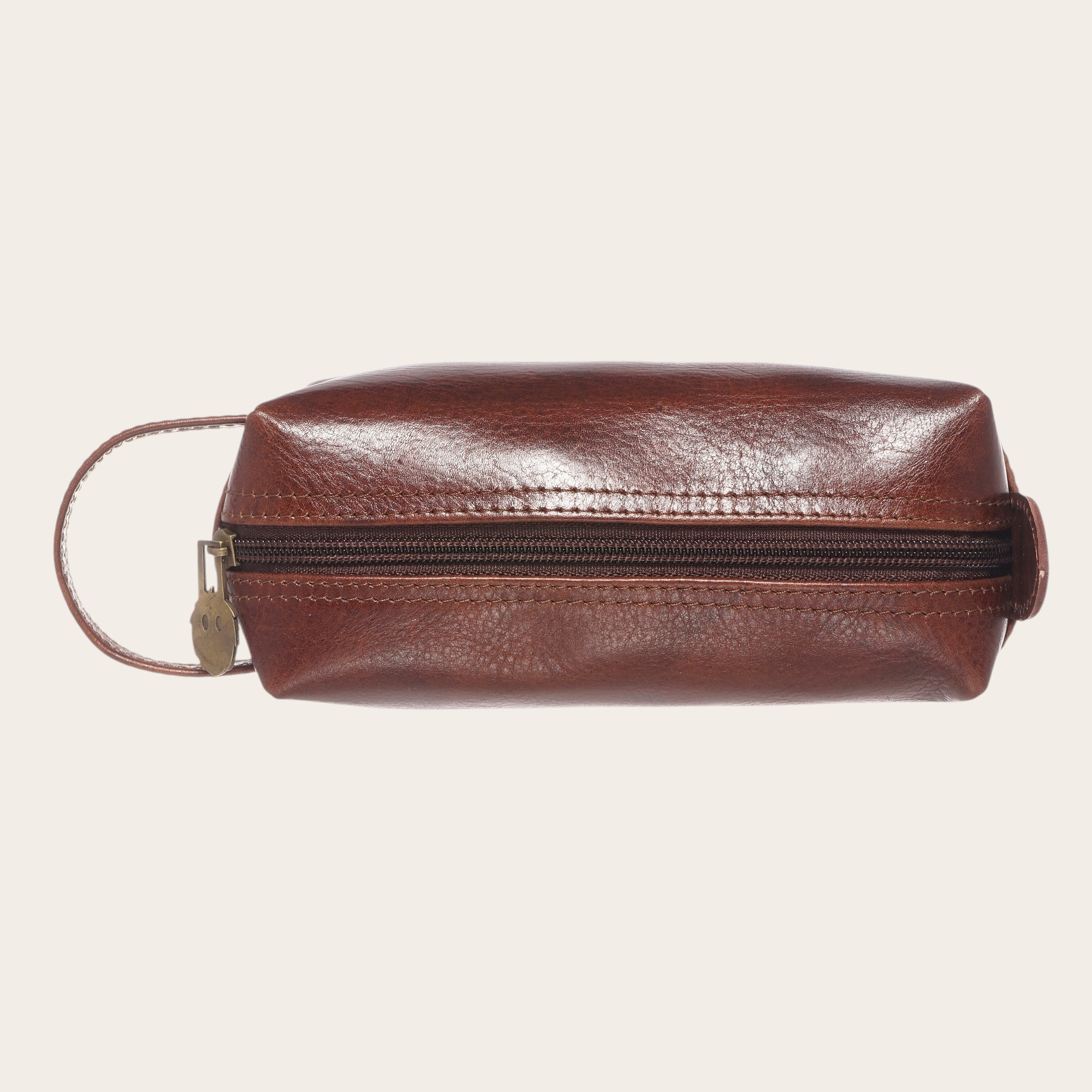 Neceser Lluta Castaño de cuero marrón de OLKI con asa lateral y cremallera dorada. Ideal para organizar artículos de aseo.