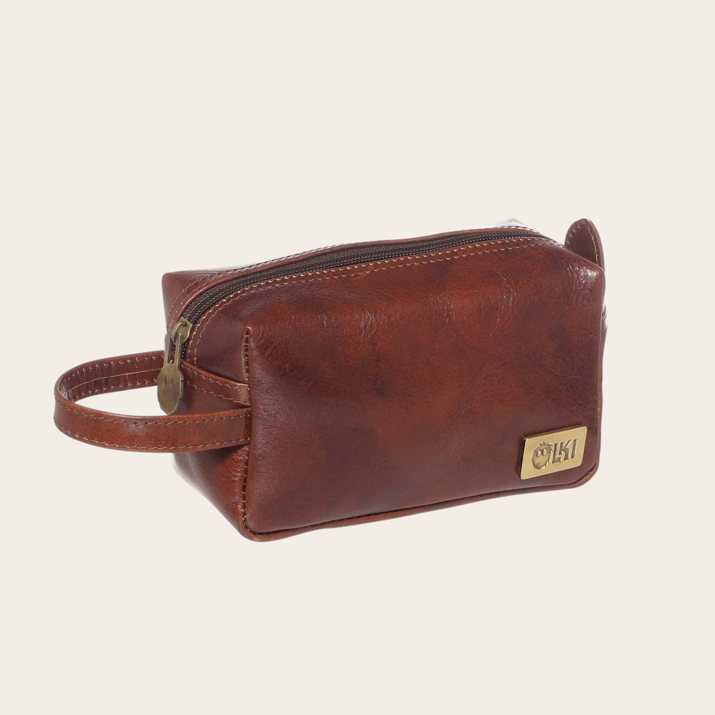 Neceser Lluta Castaño de cuero marrón de OLKI con asa lateral y cierre de cremallera. Ideal para viajes.