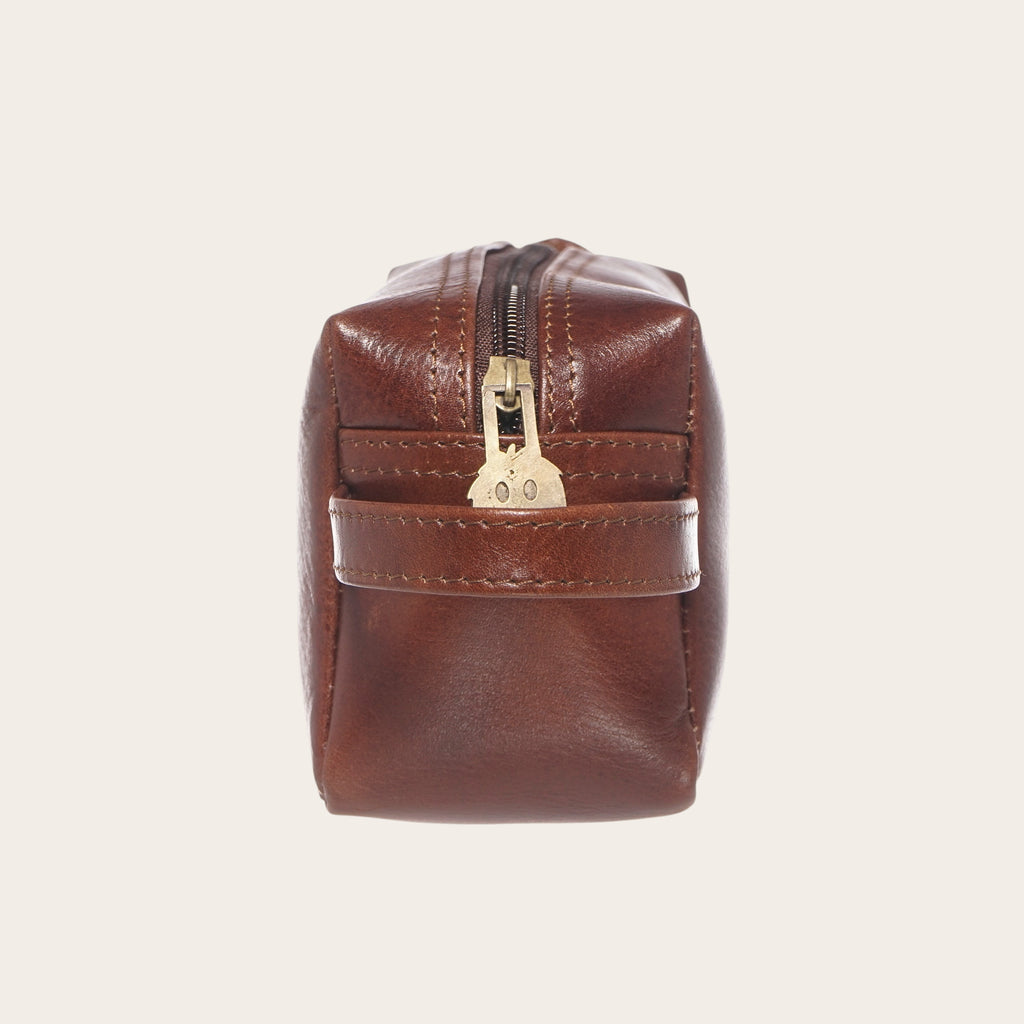 Neceser Lluta de cuero castaño de OLKI con cremallera dorada y asa lateral. Ideal para organizar artículos de aseo.