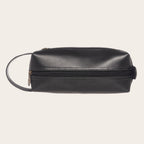Neceser de cuero negro OLKI Lluta con asa lateral, cremallera y costuras detalladas. Ideal para viaje o uso diario.