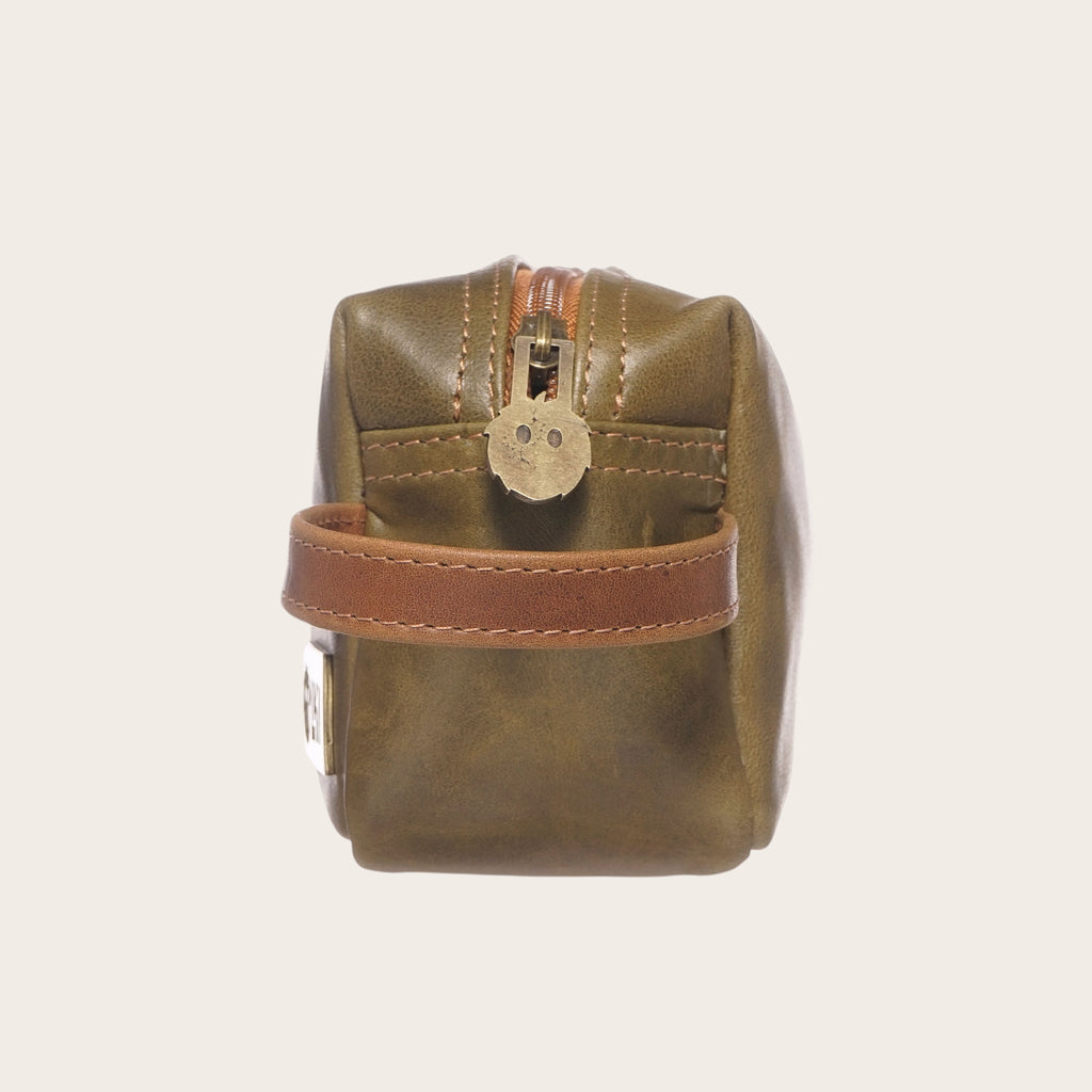 Neceser Lluta de cuero verde y caramelo de OLKI con asa lateral y tirador de cremallera con forma de cara sonriente.