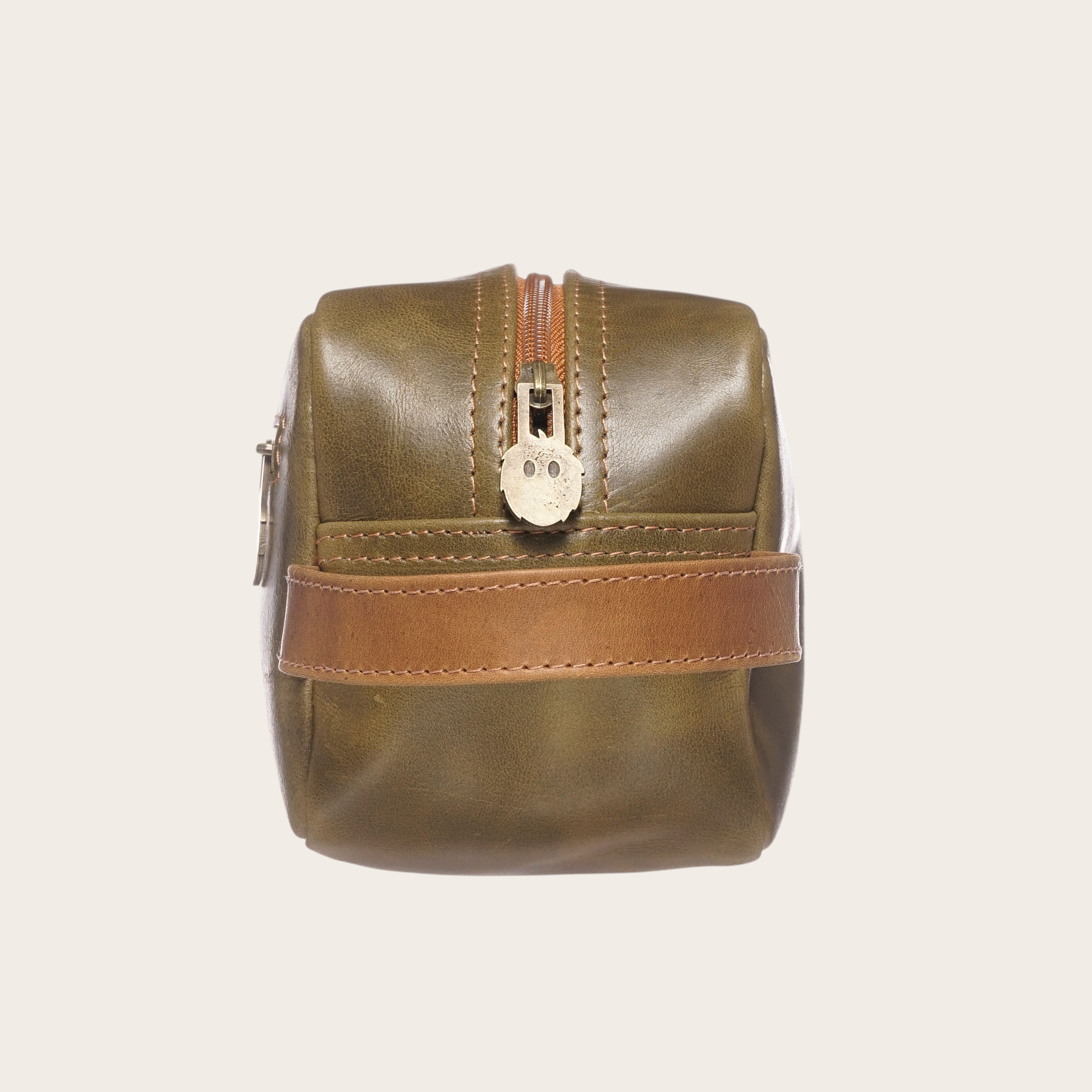 Neceser Loa Verde-Caramel de OLKI en cuero con cremallera y detalle de asa lateral.