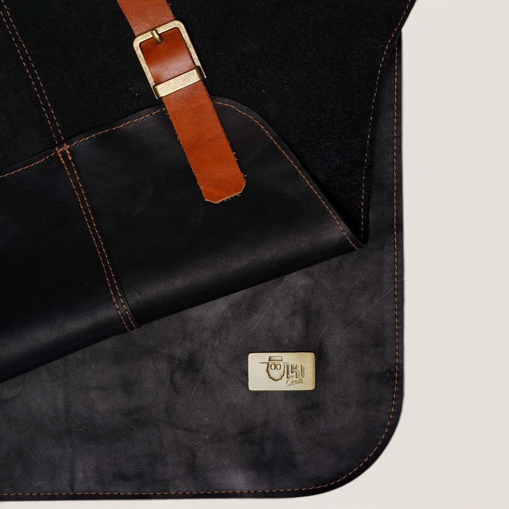 Pechera de cuero natural negro OLKI con costuras reforzadas, correa de ajuste color café y placa metálica de la marca