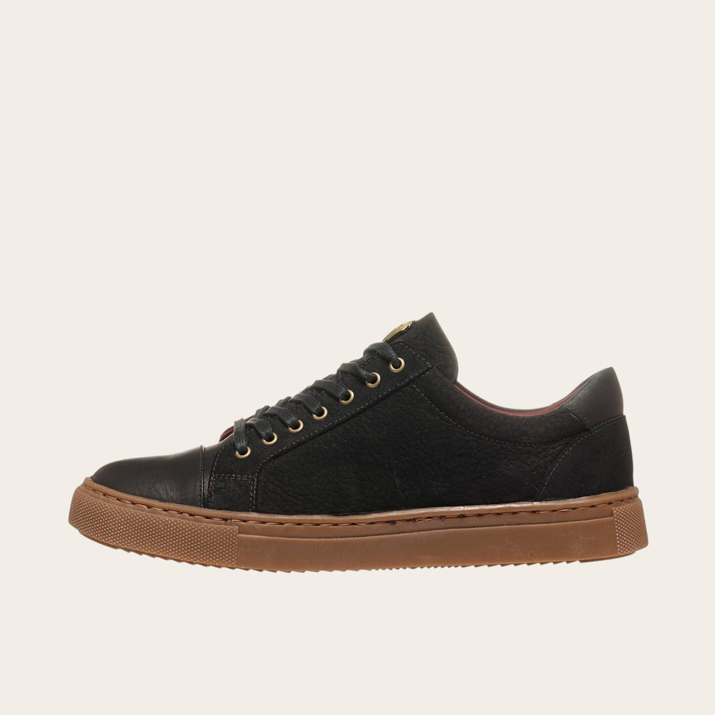 Zapatilla casual de cuero OLKI negra con detalles camel y suela de goma marrón.