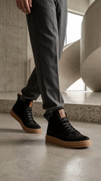 Zapatilla alta negra de Nobuk de OLKI con suela de goma marrón y cordones negros. Diseño urbano.